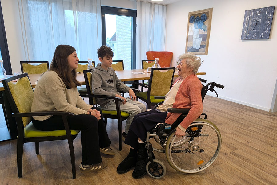 „Jung und Alt“ tauschen Erfahrungen aus: zwei Konfirmanden sprechen mit einer Heimbewohnerin im Rollstuhl